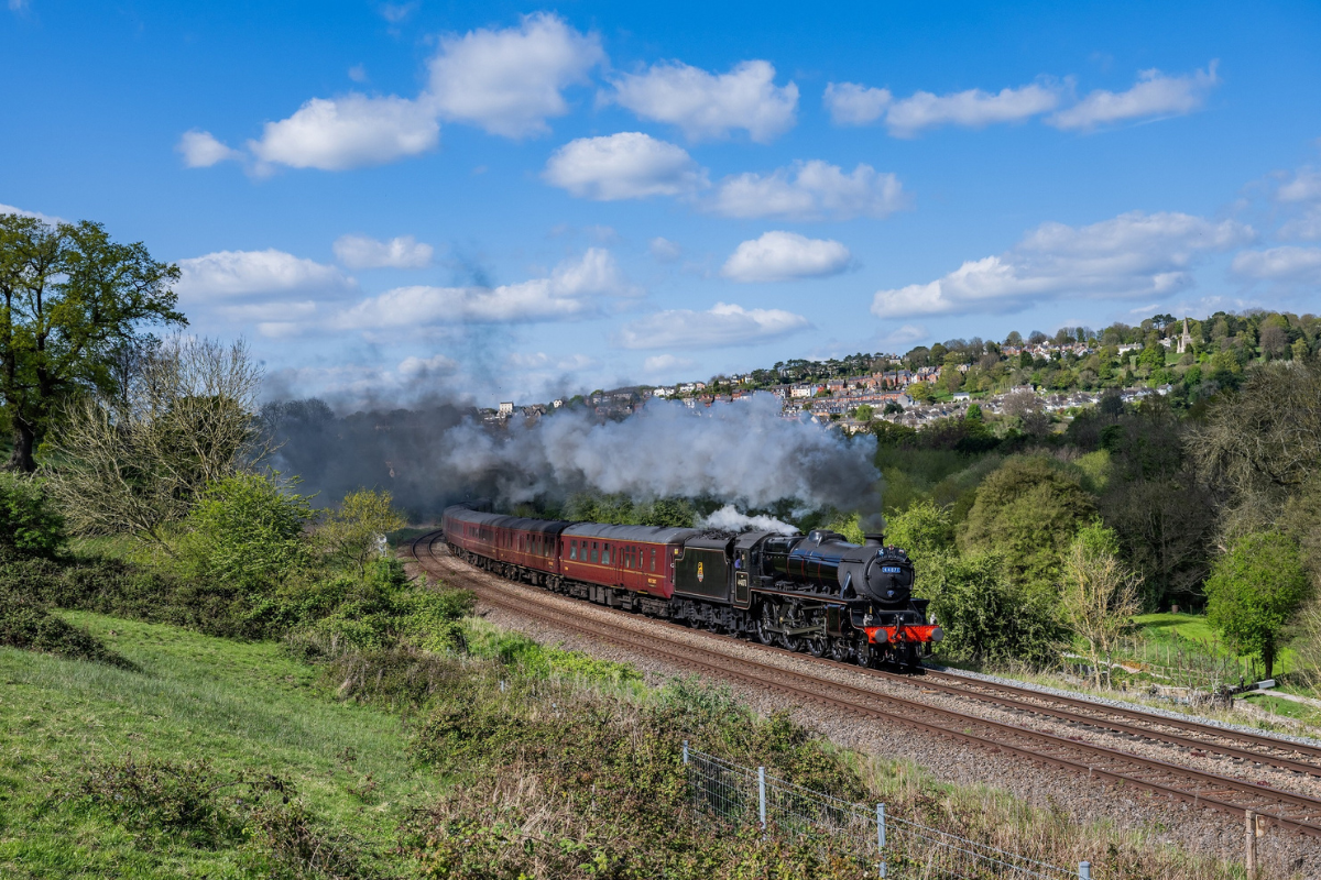 A steam train winds through picturesque countryside on a sunny day.