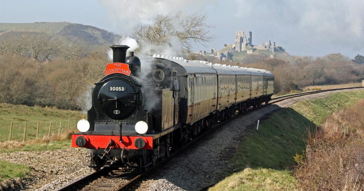 A vintage steam train chugs through the scenic Dorset countryside, with a historic castle in the background.