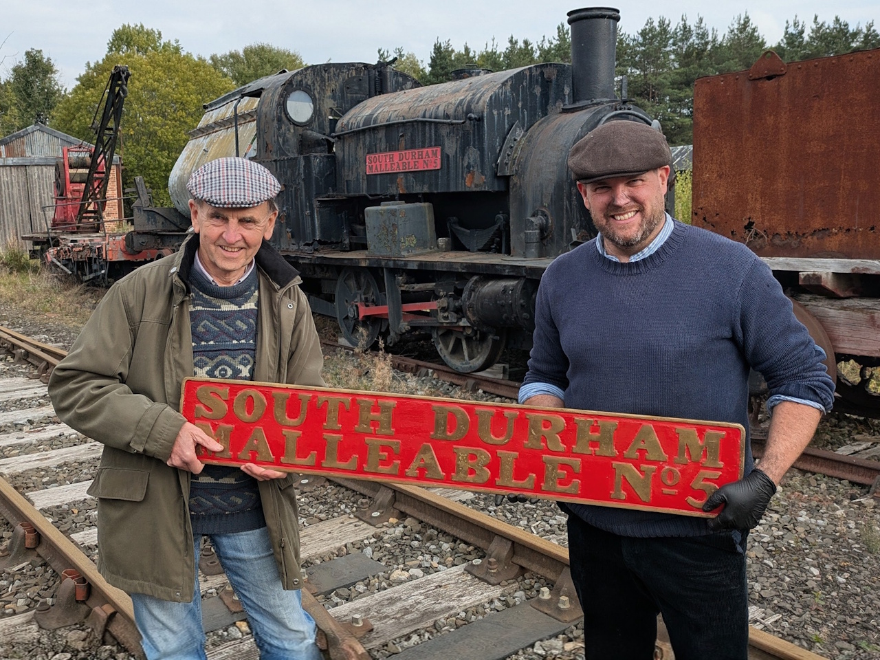 Restoring history: Proudly holding the South Durham Mallearble No. 5 sign near the vintage locomotive.